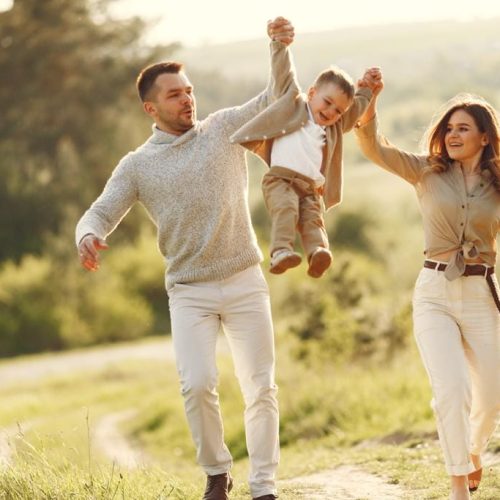 Loving parents swinging their son by his arms in summer field